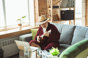 Image showing Mature senior older man during quarantine, realizing how important stay at home during virus outbreak, giving concert of taking online lessons of guitar playing