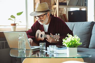 Image showing Mature senior older man during quarantine, realizing how important stay at home during virus outbreak, giving concert of taking online lessons of guitar playing