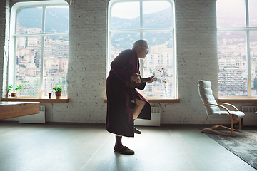 Image showing Mature senior older man during quarantine, realizing how important stay at home during virus outbreak, giving concert of taking online lessons of guitar playing in Monte Carlo