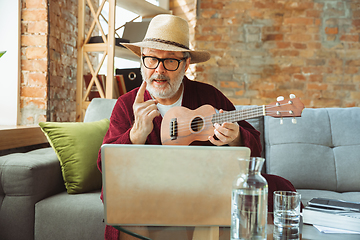 Image showing Mature senior older man during quarantine, realizing how important stay at home during virus outbreak, giving concert of taking online lessons of guitar playing