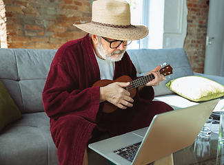 Image showing Mature senior older man during quarantine, realizing how important stay at home during virus outbreak, giving concert of taking online lessons of guitar playing