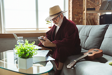 Image showing Mature senior older man during quarantine, realizing how important stay at home during virus outbreak, giving concert of taking online lessons of guitar playing