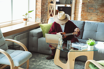 Image showing Mature senior older man during quarantine, realizing how important stay at home during virus outbreak, giving concert of taking online lessons of guitar playing