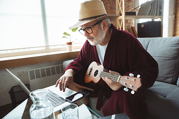 Image showing Mature senior older man during quarantine, realizing how important stay at home during virus outbreak, giving concert of taking online lessons of guitar playing