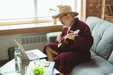 Image showing Mature senior older man during quarantine, realizing how important stay at home during virus outbreak, giving concert of taking online lessons of guitar playing