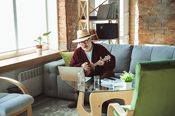 Image showing Mature senior older man during quarantine, realizing how important stay at home during virus outbreak, giving concert of taking online lessons of guitar playing