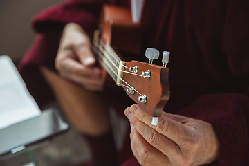 Image showing Mature senior older man during quarantine, virus outbreak, giving concert of taking online lessons of guitar playing, close up of hands