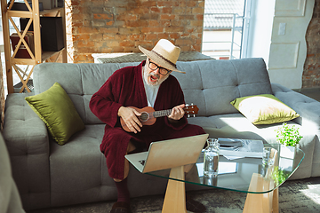 Image showing Mature senior older man during quarantine, realizing how important stay at home during virus outbreak, giving concert of taking online lessons of guitar playing