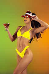 Image showing Fashion portrait of young fit and sportive woman with cocktail in stylish yellow luxury swimwear on gradient background. Perfect body ready for summertime.