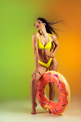 Image showing Fashion portrait of young fit and sportive woman with rubber donut in stylish yellow swimwear on gradient background. Perfect body ready for summertime.