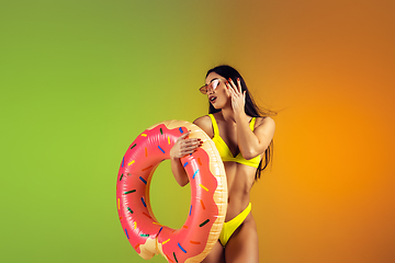 Image showing Fashion portrait of young fit and sportive woman with rubber donut in stylish yellow swimwear on gradient background. Perfect body ready for summertime.