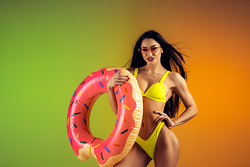 Image showing Fashion portrait of young fit and sportive woman with rubber donut in stylish yellow swimwear on gradient background. Perfect body ready for summertime.