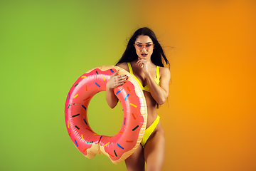 Image showing Fashion portrait of young fit and sportive woman with rubber donut in stylish yellow swimwear on gradient background. Perfect body ready for summertime.