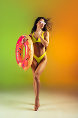 Image showing Fashion portrait of young fit and sportive woman with rubber donut in stylish yellow swimwear on gradient background. Perfect body ready for summertime.