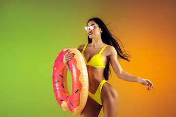 Image showing Fashion portrait of young fit and sportive woman with rubber donut in stylish yellow swimwear on gradient background. Perfect body ready for summertime.