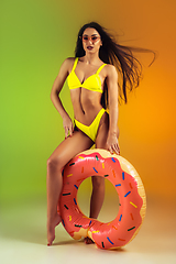 Image showing Fashion portrait of young fit and sportive woman with rubber donut in stylish yellow swimwear on gradient background. Perfect body ready for summertime.