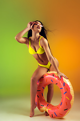 Image showing Fashion portrait of young fit and sportive woman with rubber donut in stylish yellow swimwear on gradient background. Perfect body ready for summertime.