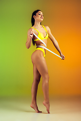 Image showing Close up of young fit and sportive woman with measurer in stylish yellow swimwear on gradient background. Perfect body ready for summertime.