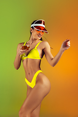 Image showing Fashion portrait of young fit and sportive woman with cocktail in stylish yellow luxury swimwear on gradient background. Perfect body ready for summertime.