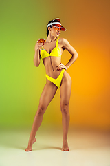 Image showing Fashion portrait of young fit and sportive woman with cocktail in stylish yellow luxury swimwear on gradient background. Perfect body ready for summertime.