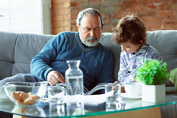 Image showing Grandfather and his grandson spending time insulated at home, having fun, reading magazine together, happy