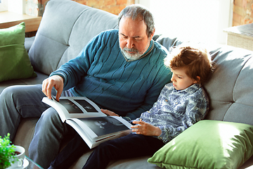 Image showing Grandfather and his grandson spending time insulated at home, having fun, reading magazine together, happy