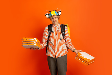 Image showing Contacless delivery service during quarantine. Man delivers food and shopping bags during insulation. Emotions of deliveryman isolated on orange background.