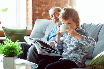 Image showing Grandfather and his grandson spending time insulated at home, having fun, reading magazine together, happy