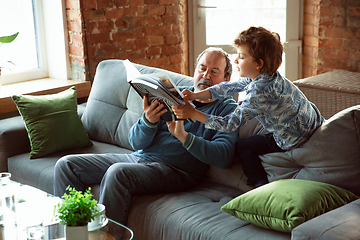 Image showing Grandfather and his grandson spending time insulated at home, having fun, reading magazine together, happy