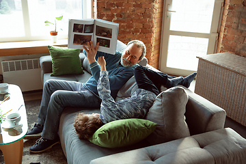 Image showing Grandfather and his grandson spending time insulated at home, having fun, reading magazine together, happy