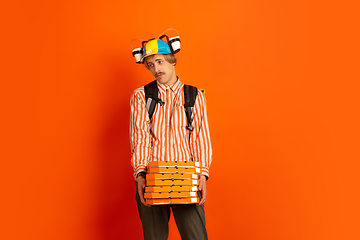 Image showing Contacless delivery service during quarantine. Man delivers food and shopping bags during insulation. Emotions of deliveryman isolated on orange background.