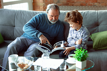 Image showing Grandfather and his grandson spending time insulated at home, having fun, reading magazine together, happy