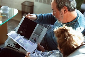 Image showing Grandfather and his grandson spending time insulated at home, having fun, reading magazine together, happy