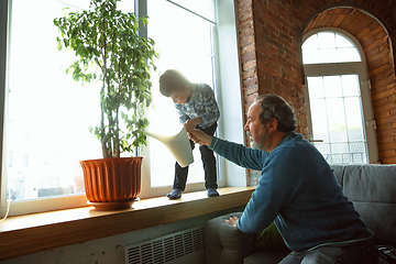 Image showing Grandfather and his grandson spending time insulated at home, having fun, caring for plants, watering