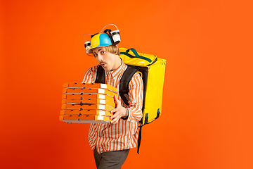 Image showing Contacless delivery service during quarantine. Man delivers food and shopping bags during insulation. Emotions of deliveryman isolated on orange background.