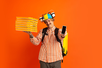 Image showing Contacless delivery service during quarantine. Man delivers food and shopping bags during insulation. Emotions of deliveryman isolated on orange background.