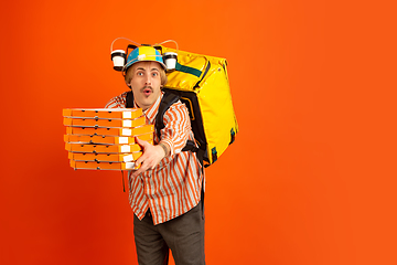 Image showing Contacless delivery service during quarantine. Man delivers food and shopping bags during insulation. Emotions of deliveryman isolated on orange background.