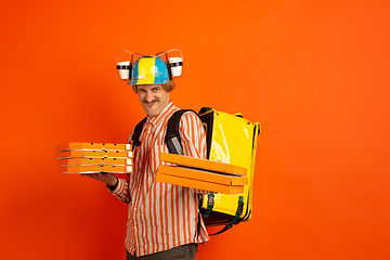 Image showing Contacless delivery service during quarantine. Man delivers food and shopping bags during insulation. Emotions of deliveryman isolated on orange background.