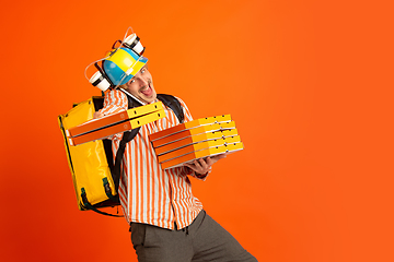 Image showing Contacless delivery service during quarantine. Man delivers food and shopping bags during insulation. Emotions of deliveryman isolated on orange background.