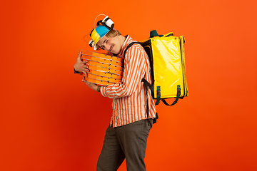 Image showing Contacless delivery service during quarantine. Man delivers food and shopping bags during insulation. Emotions of deliveryman isolated on orange background.