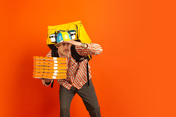 Image showing Contacless delivery service during quarantine. Man delivers food and shopping bags during insulation. Emotions of deliveryman isolated on orange background.