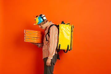 Image showing Contacless delivery service during quarantine. Man delivers food and shopping bags during insulation. Emotions of deliveryman isolated on orange background.