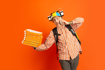 Image showing Contacless delivery service during quarantine. Man delivers food and shopping bags during insulation. Emotions of deliveryman isolated on orange background.