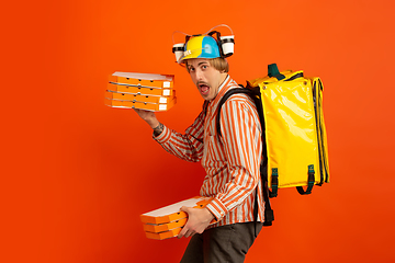 Image showing Contacless delivery service during quarantine. Man delivers food and shopping bags during insulation. Emotions of deliveryman isolated on orange background.