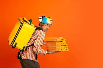 Image showing Contacless delivery service during quarantine. Man delivers food and shopping bags during insulation. Emotions of deliveryman isolated on orange background.