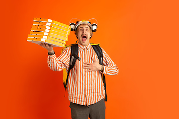 Image showing Contacless delivery service during quarantine. Man delivers food and shopping bags during insulation. Emotions of deliveryman isolated on orange background.