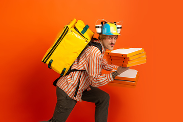 Image showing Contacless delivery service during quarantine. Man delivers food and shopping bags during insulation. Emotions of deliveryman isolated on orange background.