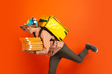 Image showing Contacless delivery service during quarantine. Man delivers food and shopping bags during insulation. Emotions of deliveryman isolated on orange background.