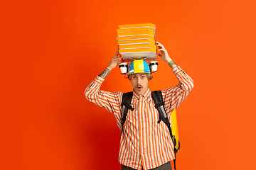 Image showing Contacless delivery service during quarantine. Man delivers food and shopping bags during insulation. Emotions of deliveryman isolated on orange background.