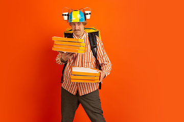 Image showing Contacless delivery service during quarantine. Man delivers food and shopping bags during insulation. Emotions of deliveryman isolated on orange background.